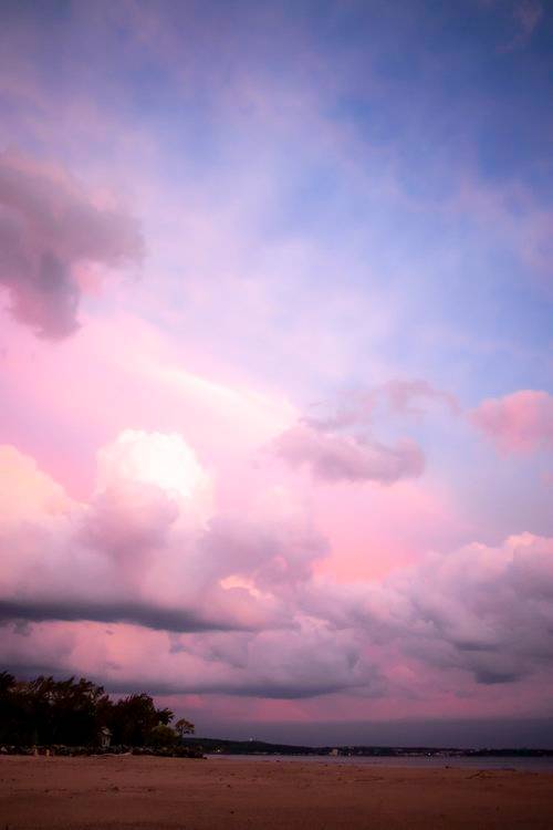 Digital photograph of a sunset with lots of purples and blues in the clouds above a body of water.